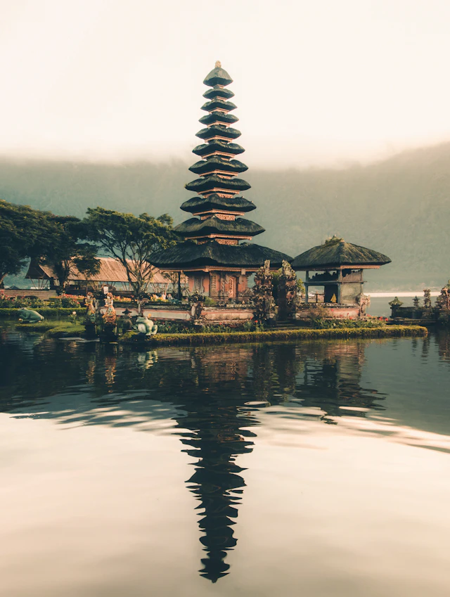 A Balinese temple reflected in a lake beneath misty green hills
